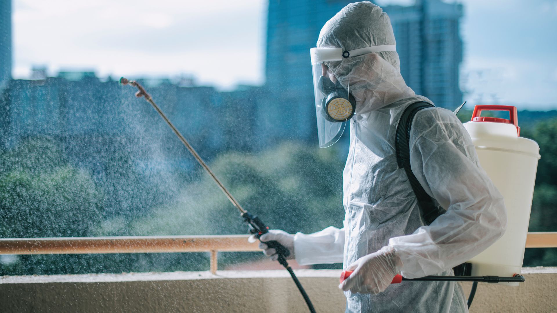 A man in a protective suit sprays disinfectant on a balcony